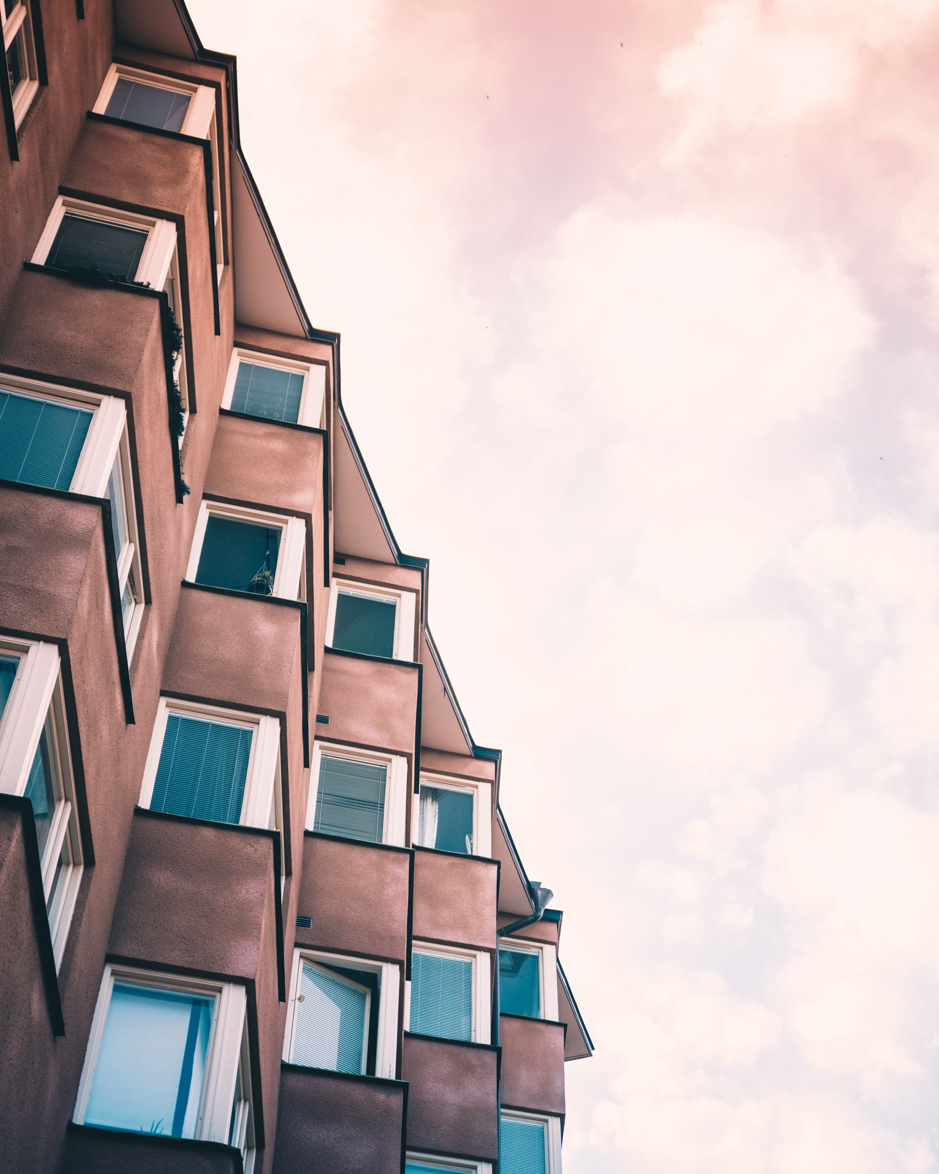 Angled windows of a brick apartment block in Stockholm against a pink evening sky