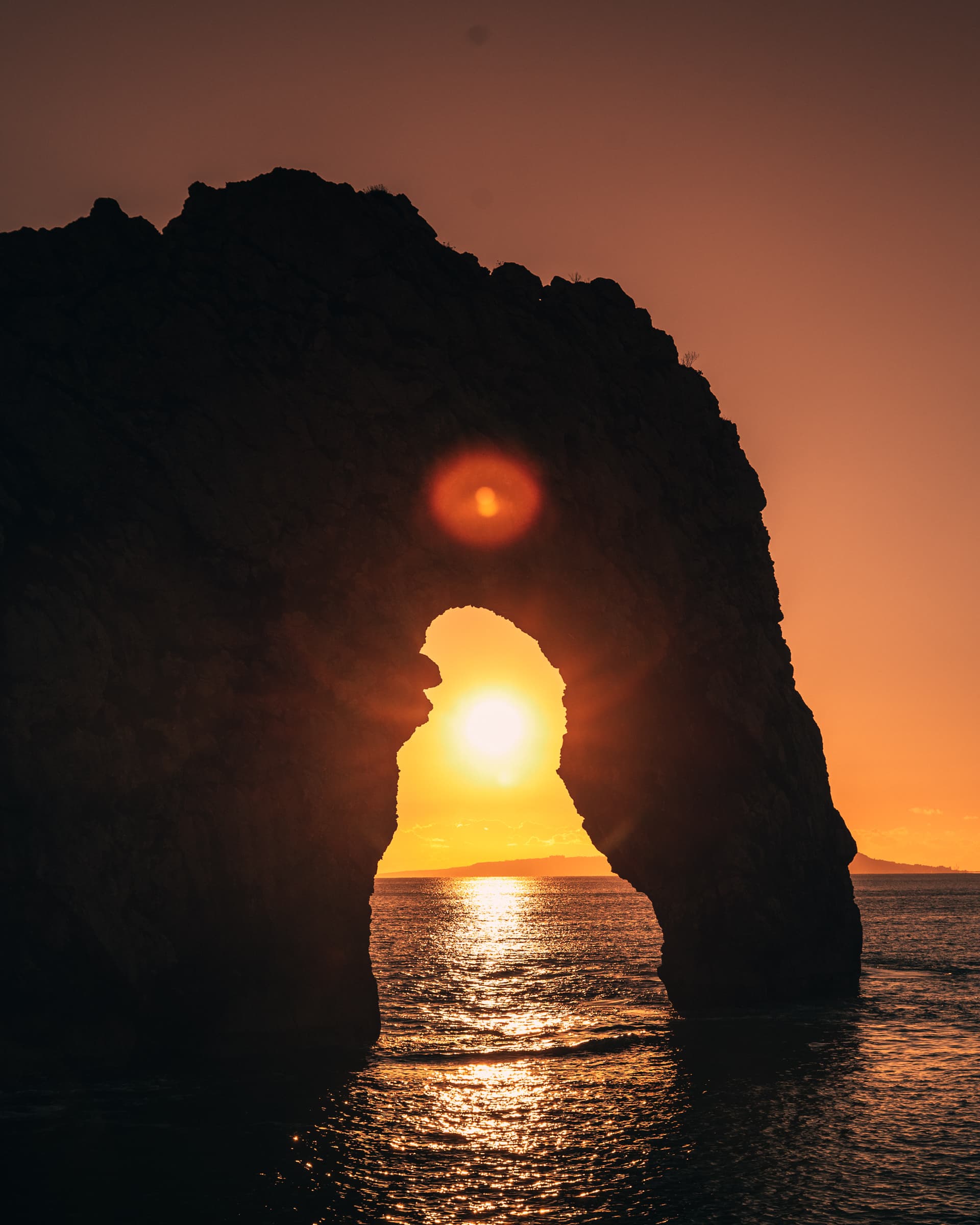 Durdle Door on the Dorset coast, the sun setting through the arch