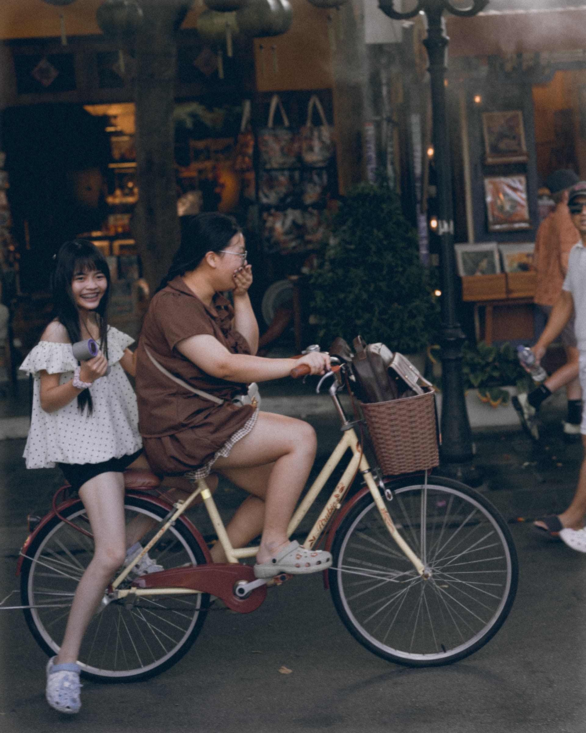 Two women riding one bicycle past shopfronts