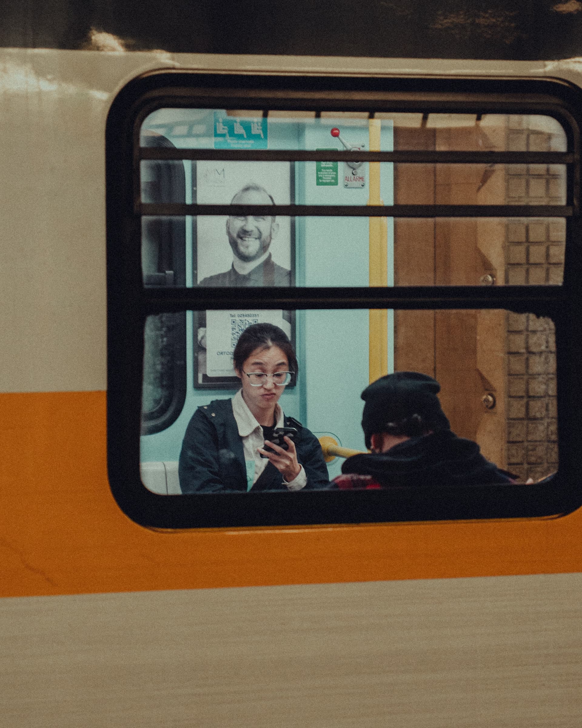 Passenger looking at her phone behind a train window with an orange stripe