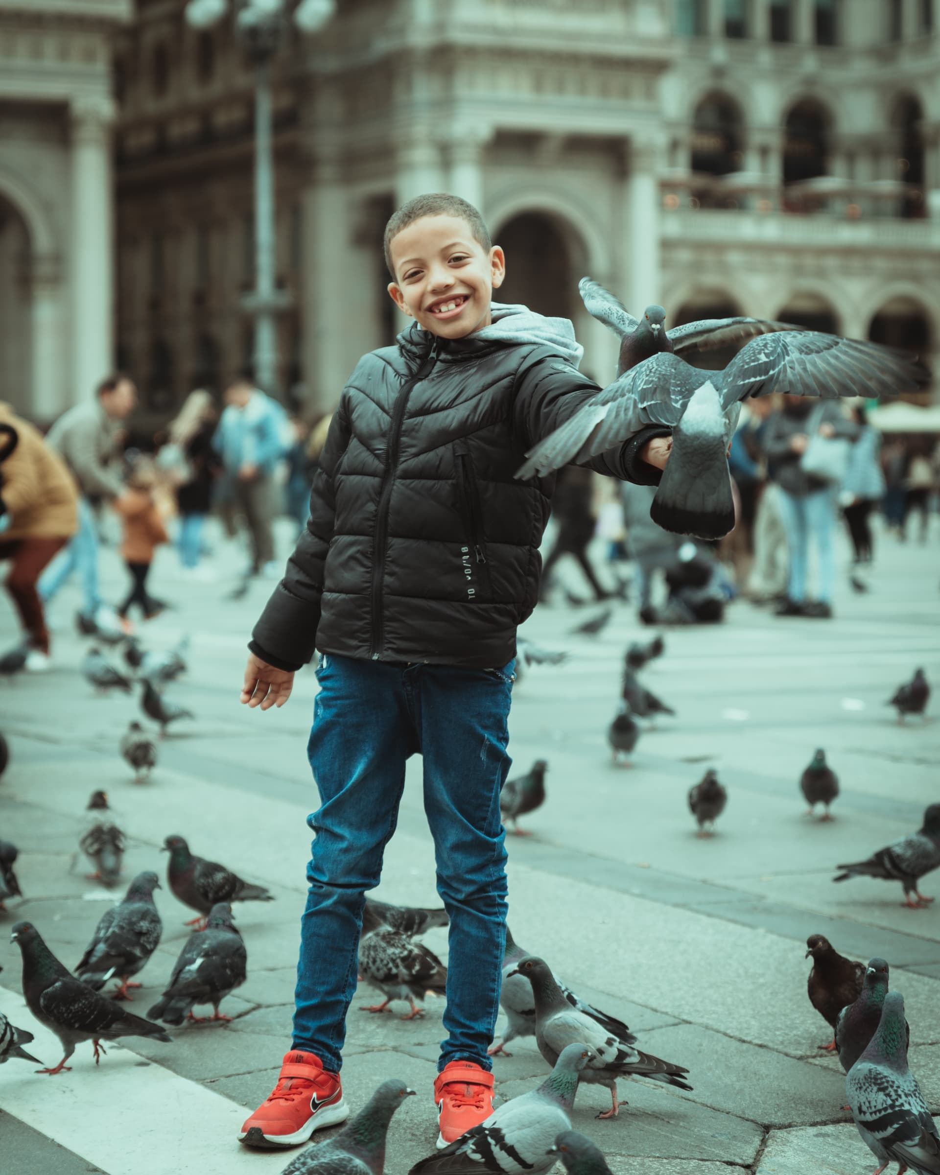 Boy laughing among pigeons in a city square