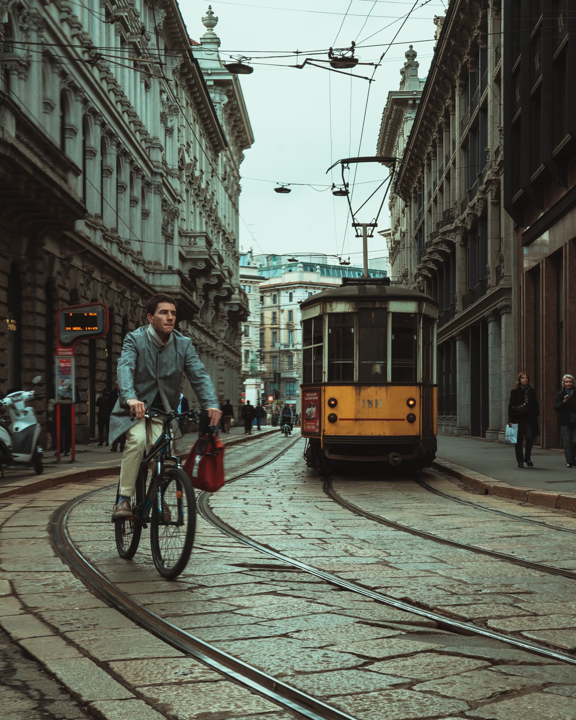 Cyclist and a yellow tram on a cobbled street in Milan