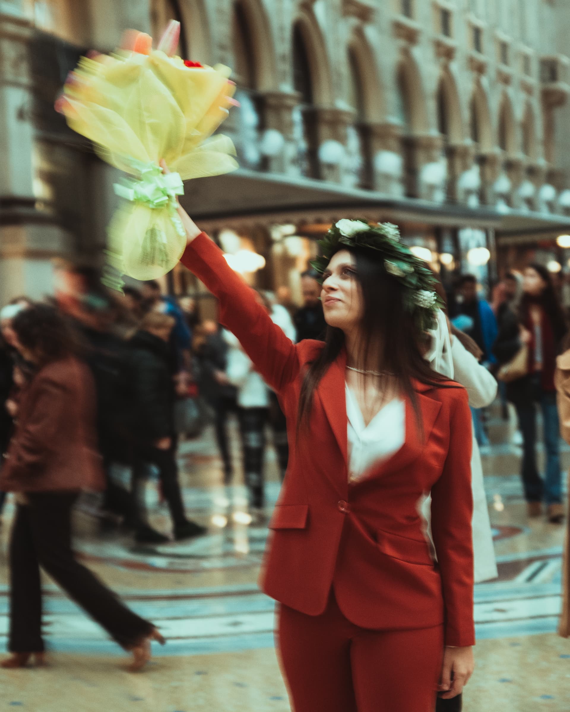 Woman in a red suit and laurel wreath raising a bouquet in the Galleria Vittorio Emanuele II, Milan